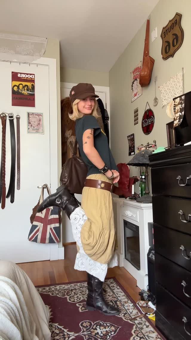 A blonde woman posing in a room wearing vintage-inspired bohemian clothing and a brown cap.