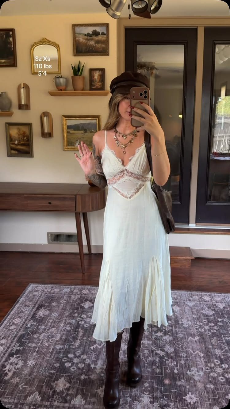 Woman in a white V-neck cami dress posing for a mirror selfie indoors.