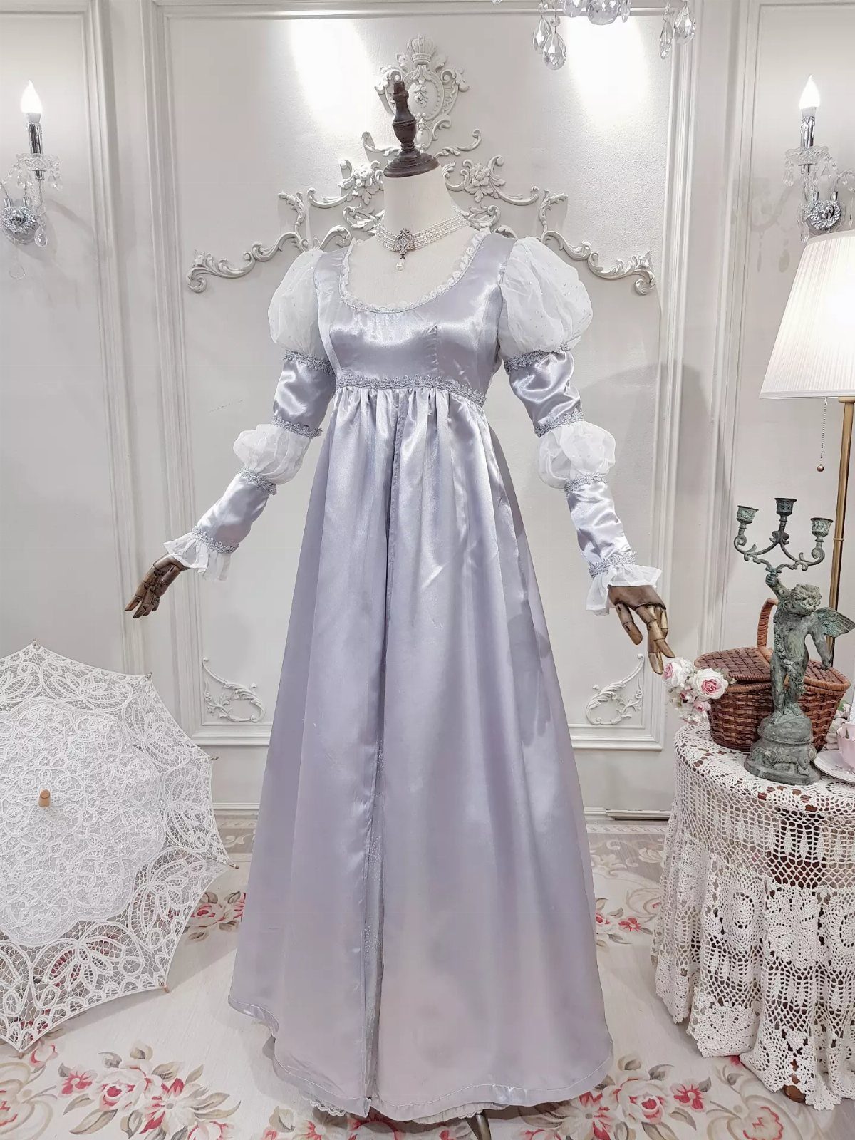 A light blue satin Regency-style dress with large white puffed sleeves on a mannequin.