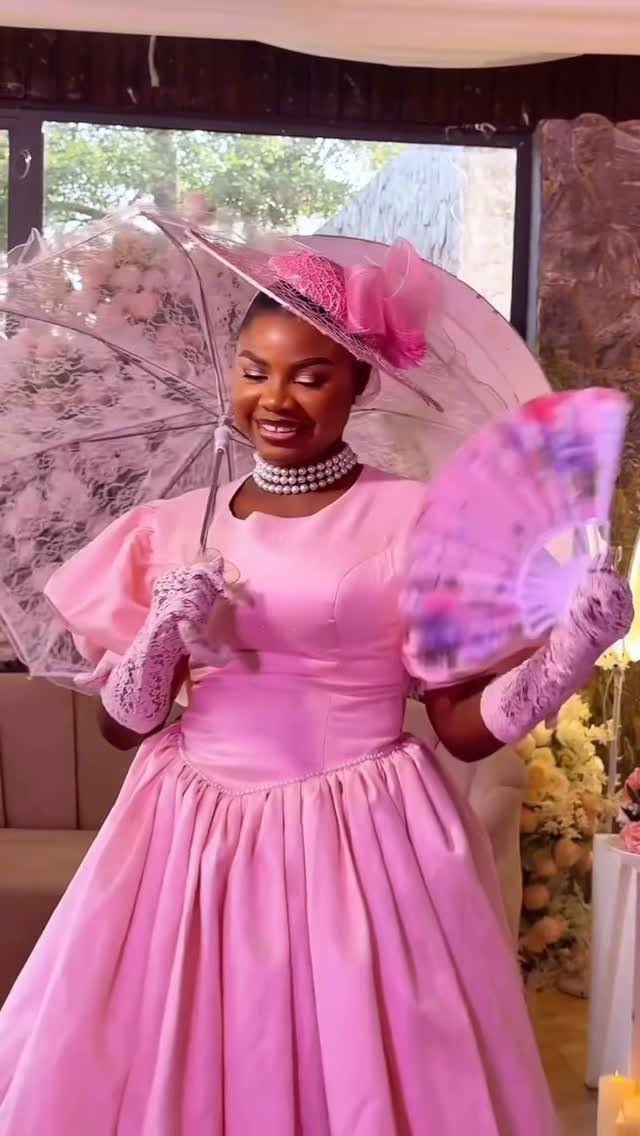 A woman in a pink Regency-style gown holding a lace parasol and a pink fan.
