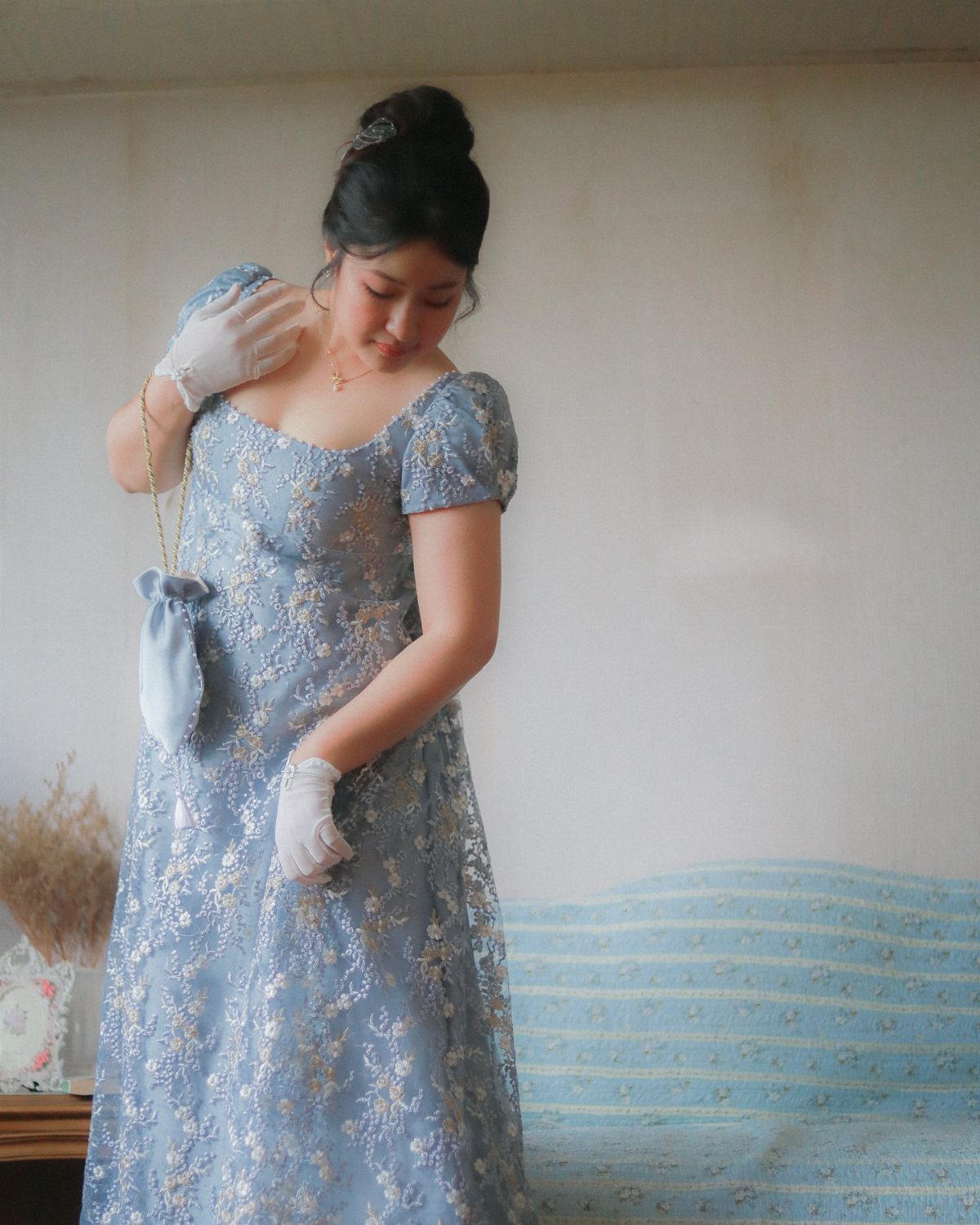 Woman in a light blue empire-waist lace dress with puff sleeves and white gloves.
