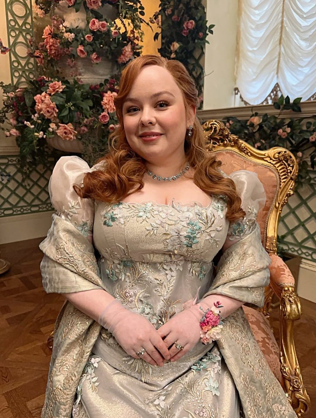 A woman in an embroidered silver Regency-style gown sitting in an ornate gold chair.