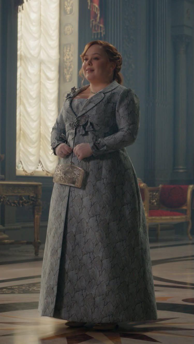 A woman in a grey patterned empire-waist jacquard gown standing in an ornate room.