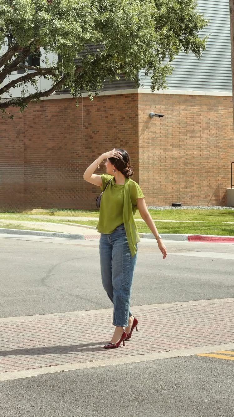 Woman in a green top and blue jeans walking in red high heels.