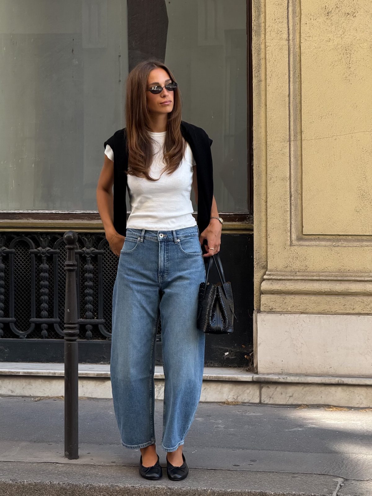 Woman wearing a white t-shirt, wide-leg blue jeans, and black ballet flats standing outdoors.