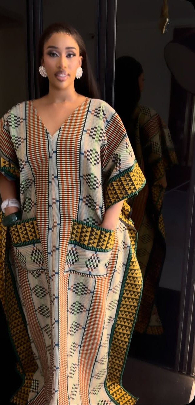 A woman posing in a colorful, patterned Ankara print kaftan dress with wide sleeves.