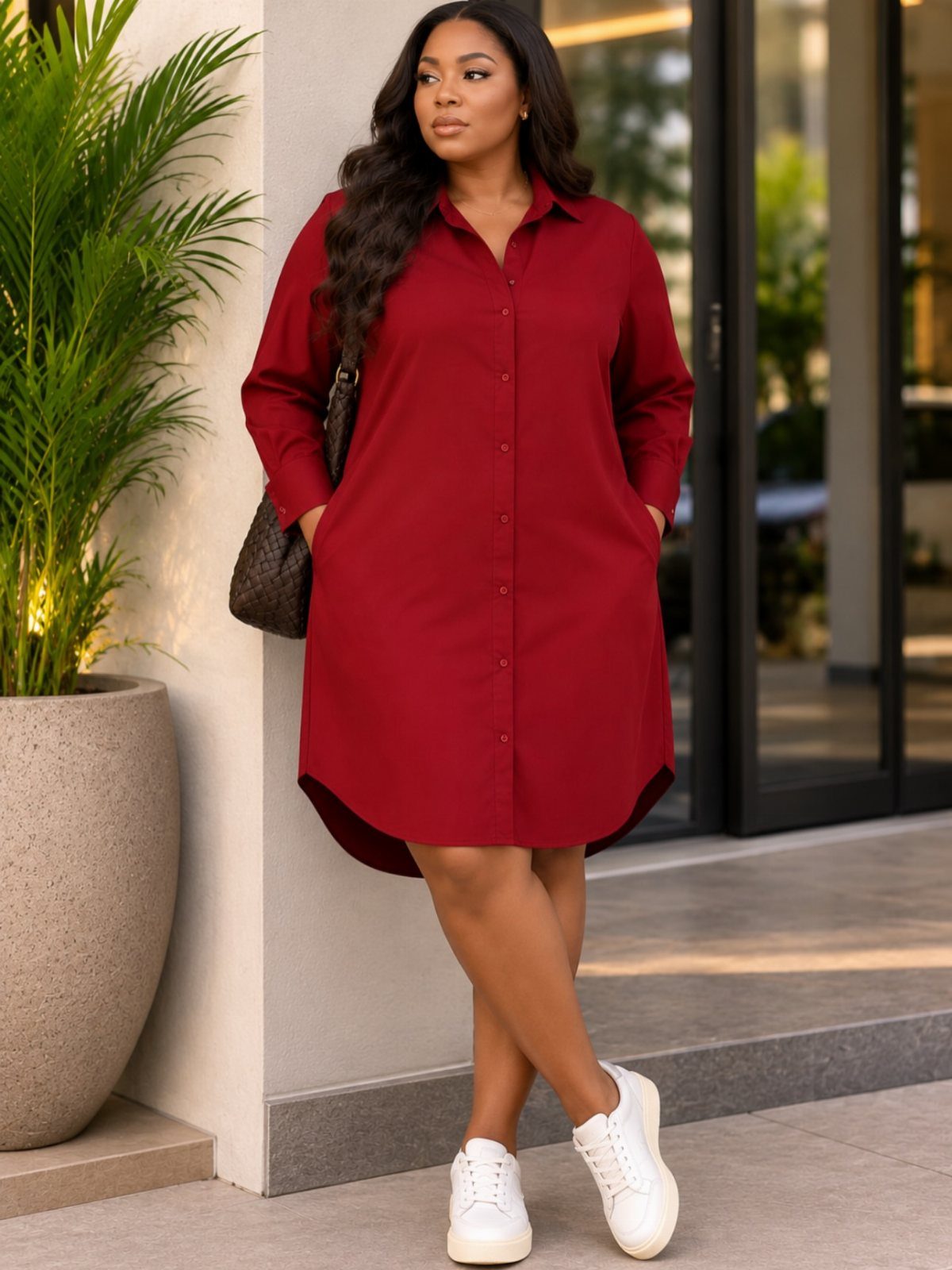 A woman wearing a long-sleeved red shirt dress and white sneakers standing outdoors.