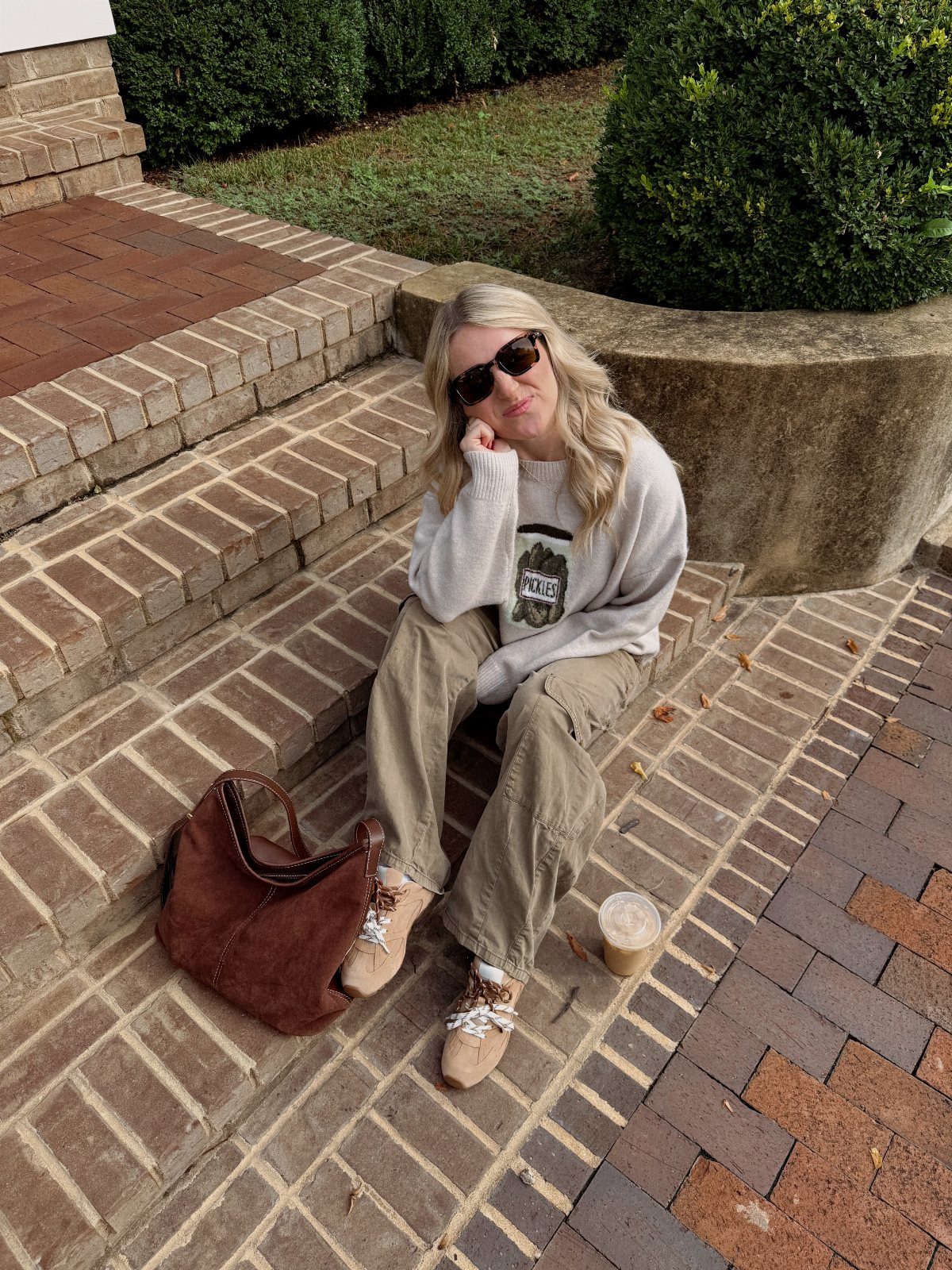Blonde woman in a grey sweater and olive cargo pants sitting on brick steps.