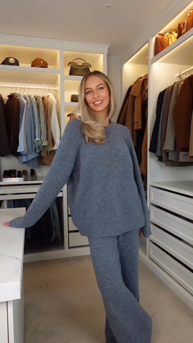 Smiling blonde woman wearing a matching blue knit crewneck sweater and wide-leg trousers in a closet.