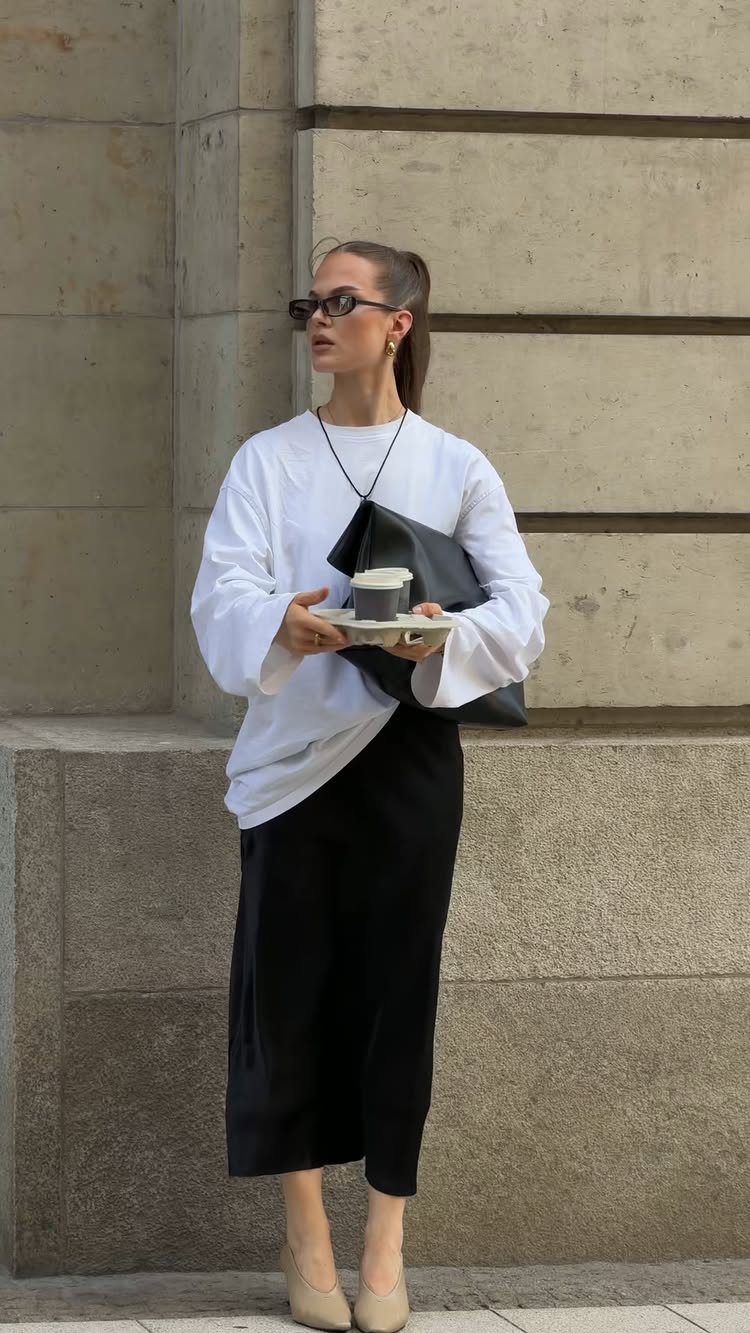 Woman wearing a white long-sleeved shirt and black silk midi skirt standing outdoors.