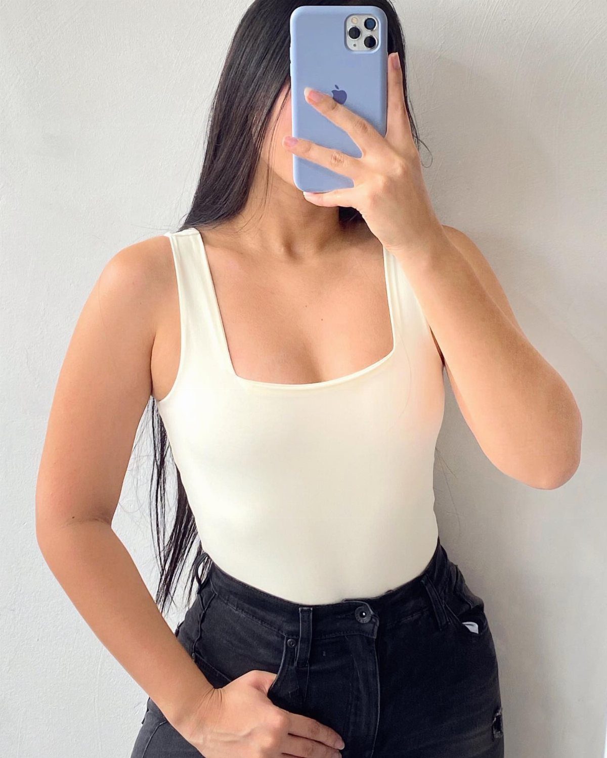 Woman in a white scoop-neck bodysuit and black jeans taking a mirror selfie.