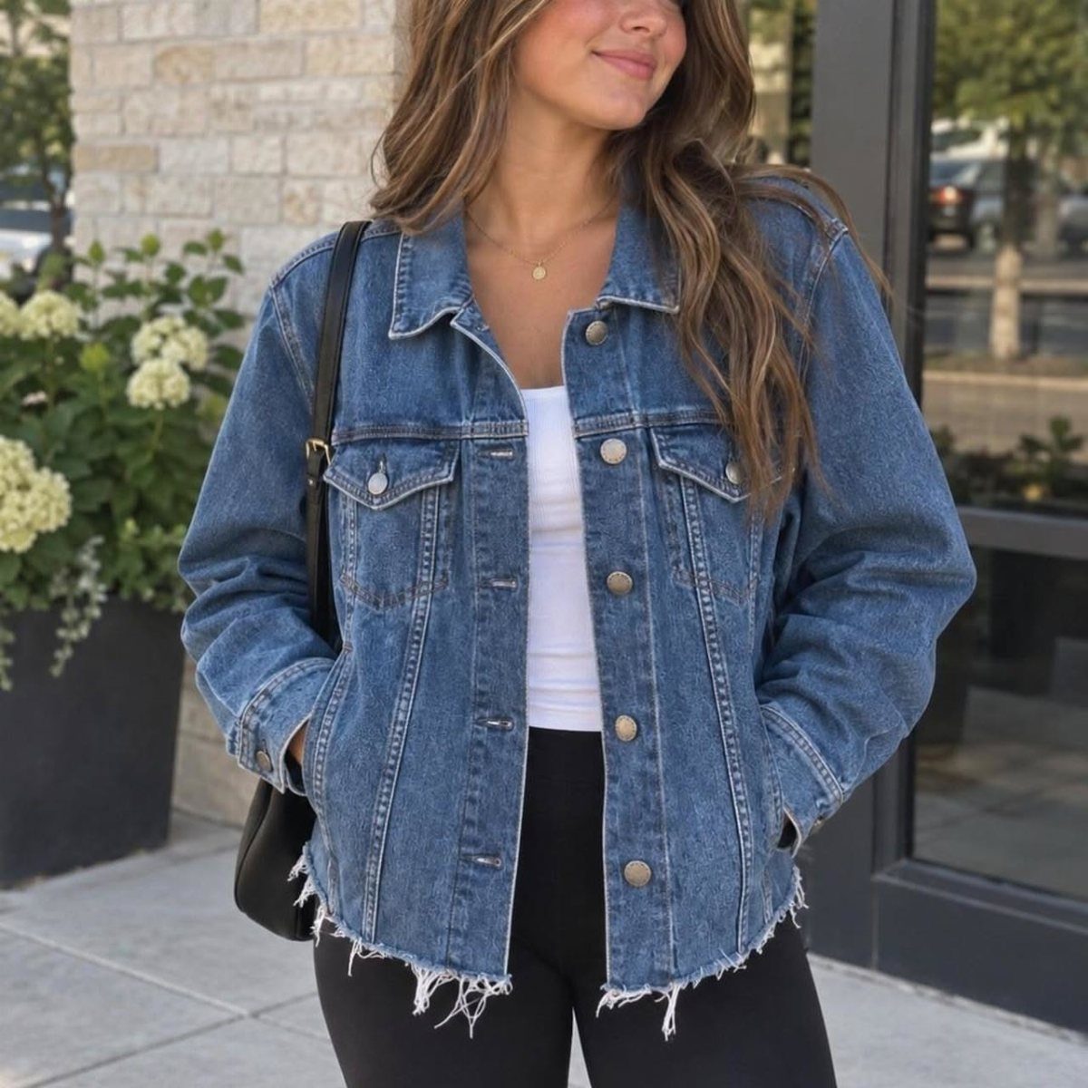 Woman wearing a blue denim jacket over a white top and black pants outdoors.