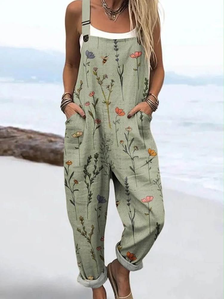 Woman wearing a sage green floral print jumpsuit standing on a sandy beach by the ocean.
