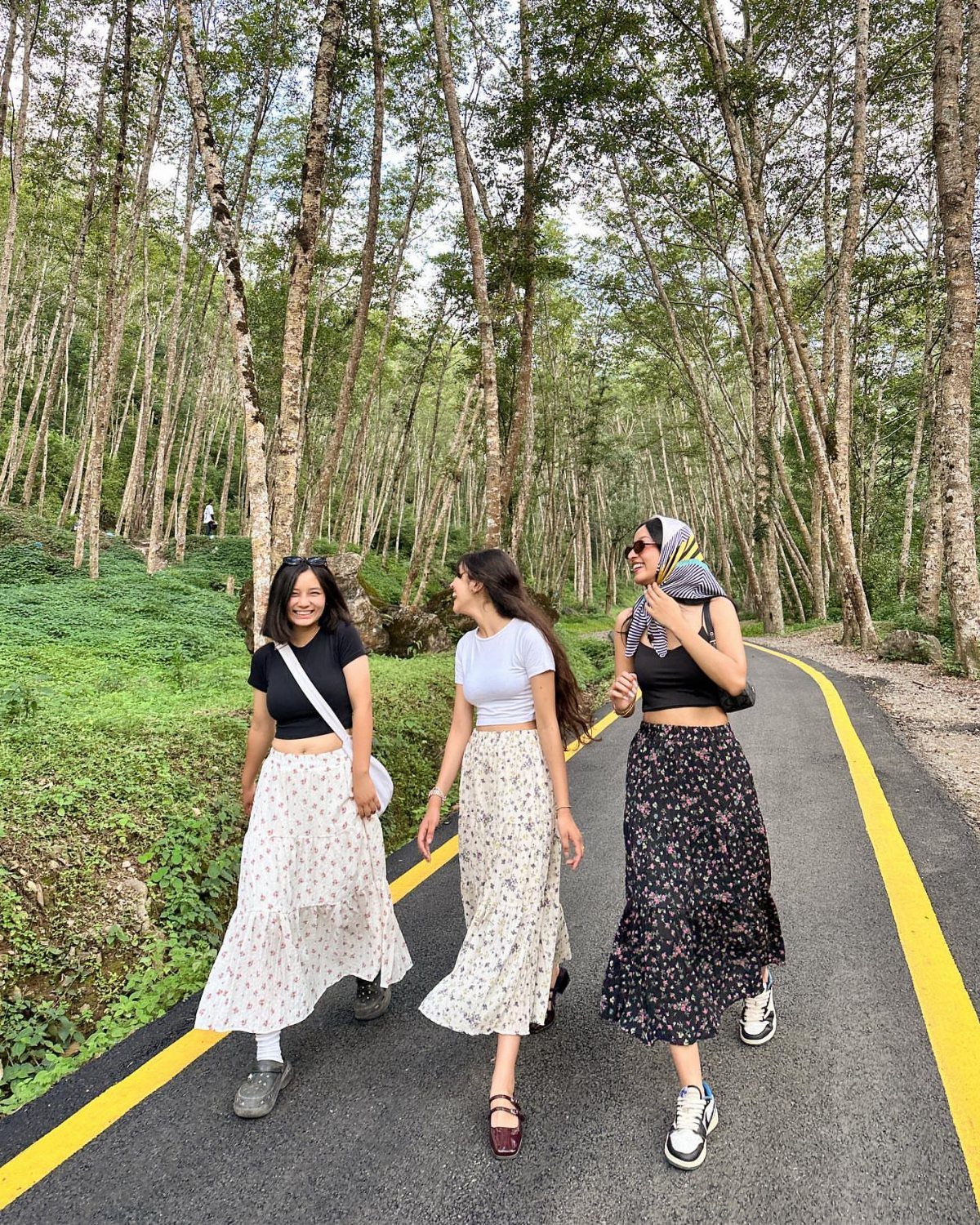 Three women walking on a forest road wearing t-shirts and long midi skirts.