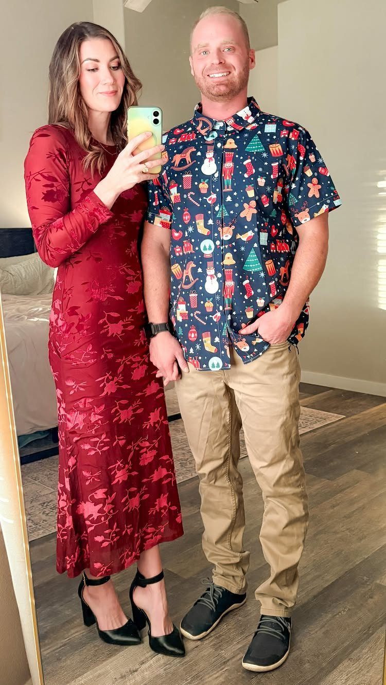 A woman in a red dress and a man in a festive Christmas shirt posing together.