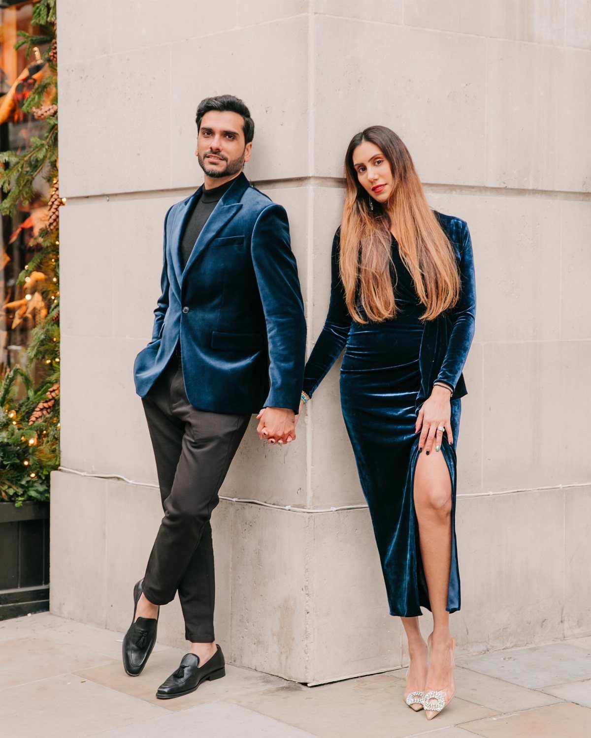 A man in a blue velvet blazer and a woman in a blue velvet dress posing outdoors.