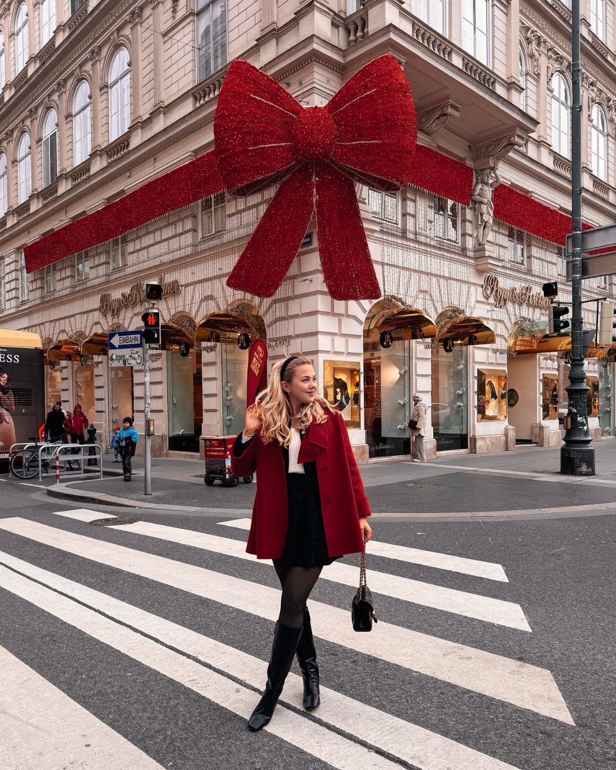 A woman in a red coat and black boots walking across a city street crosswalk.