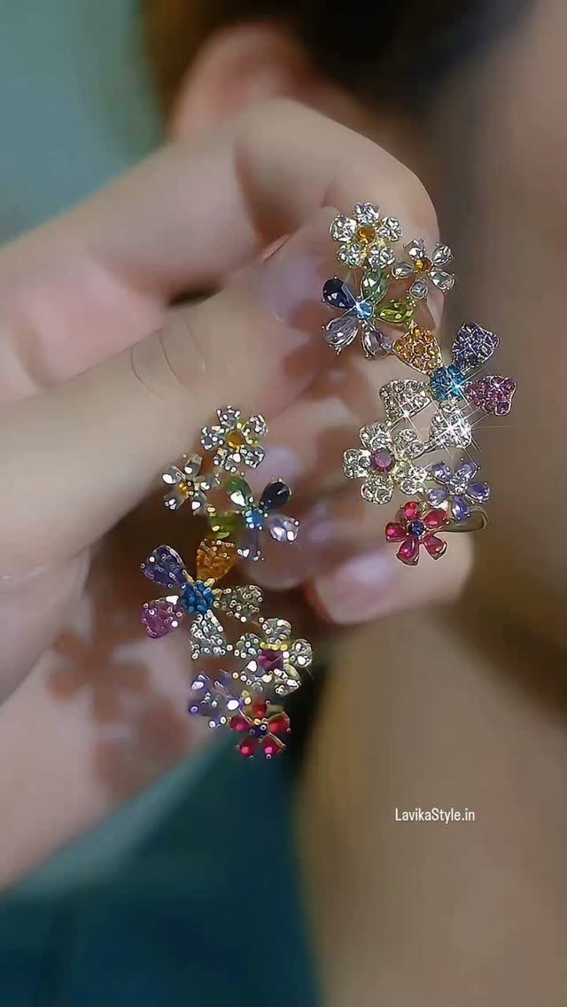 Colorful floral gemstone earrings held by a hand against a blurred background.
