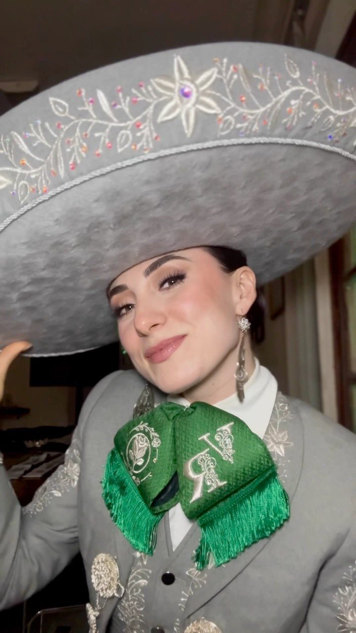 A woman smiling while wearing a large grey embroidered sombrero and a matching charro outfit.