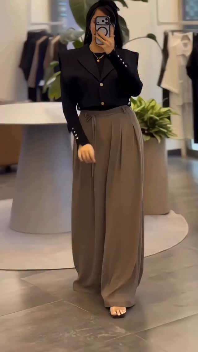 Woman in a black blazer and high-waisted wide-leg taupe trousers taking a mirror selfie.