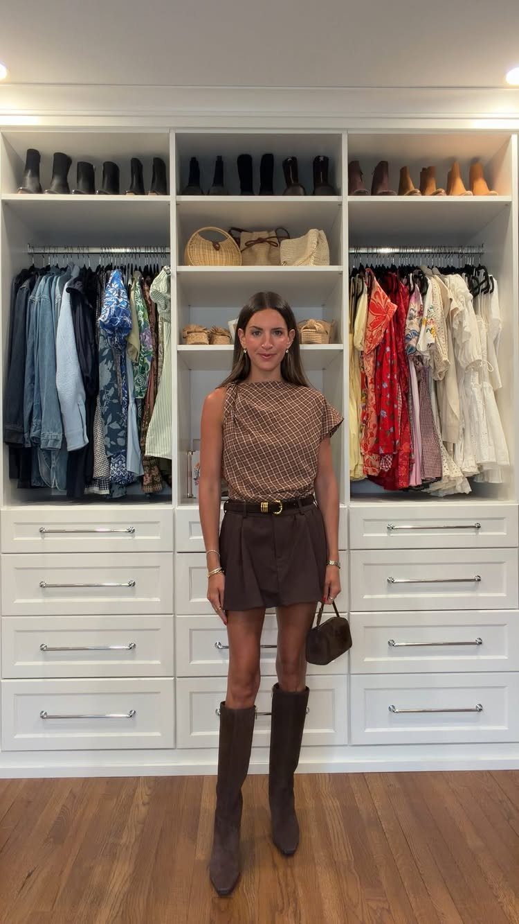 Woman wearing a brown patterned top, shorts, and brown knee-high boots in a closet.