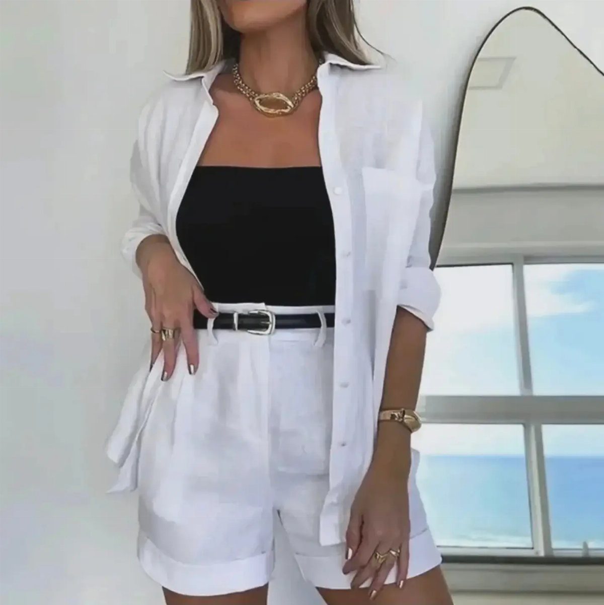 Woman wearing a white linen button-down shirt over a black top and white tailored shorts.