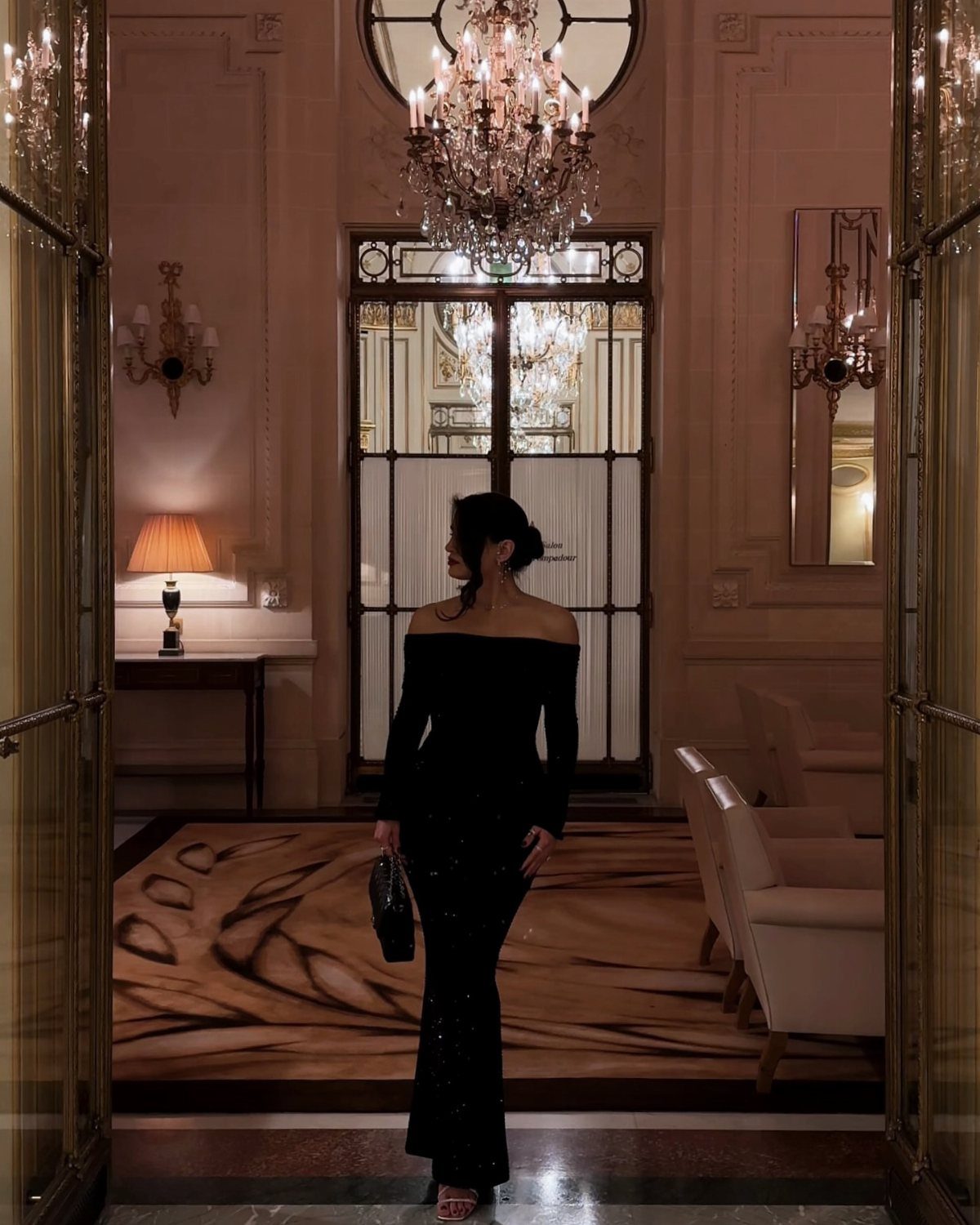 Woman in a long black off-the-shoulder evening gown standing in a luxurious room.