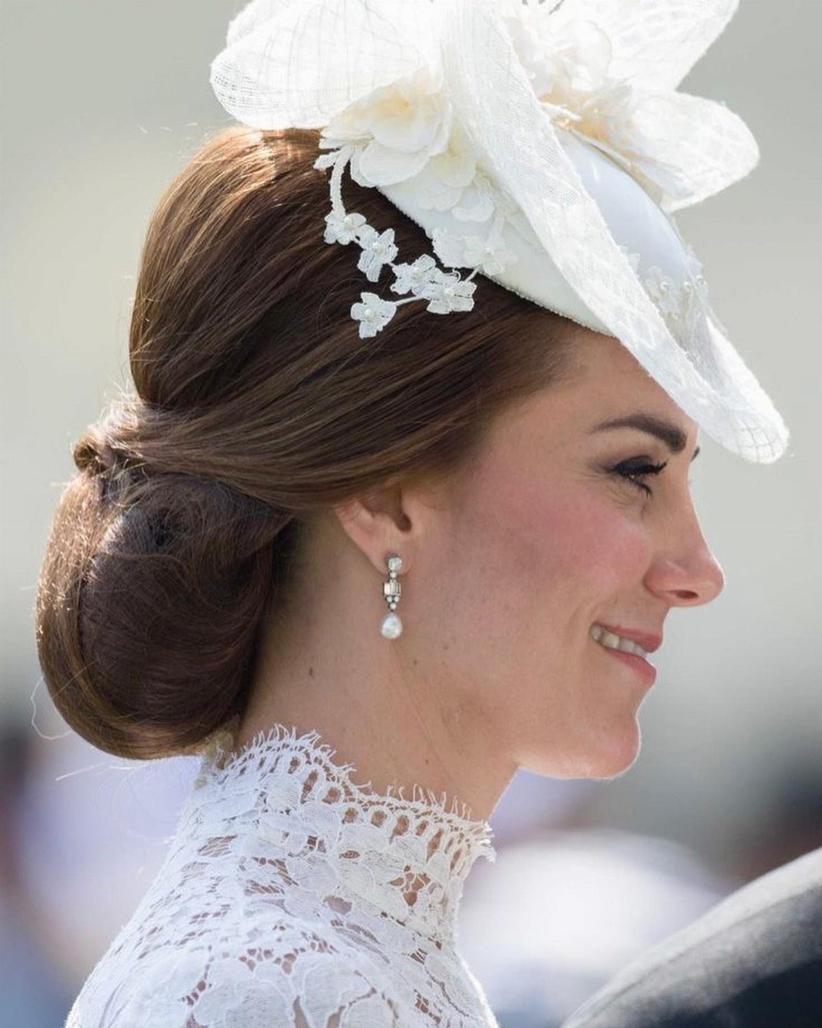A woman in profile wearing white lace clothing and elegant dangling pearl earrings.