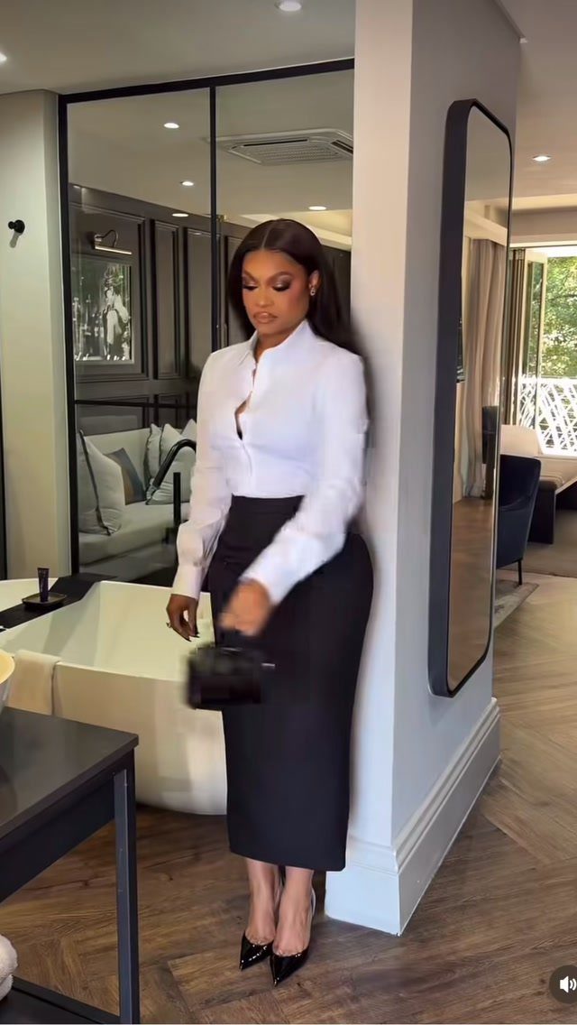 Woman in a white button-down shirt and black pencil skirt standing in a modern room.
