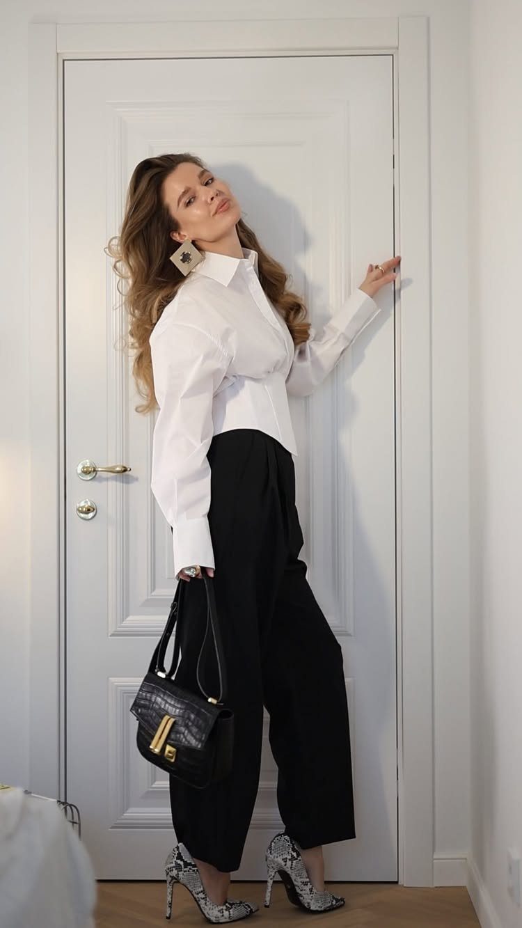 A woman posing in a white shirt and black wide-leg tailored trousers.