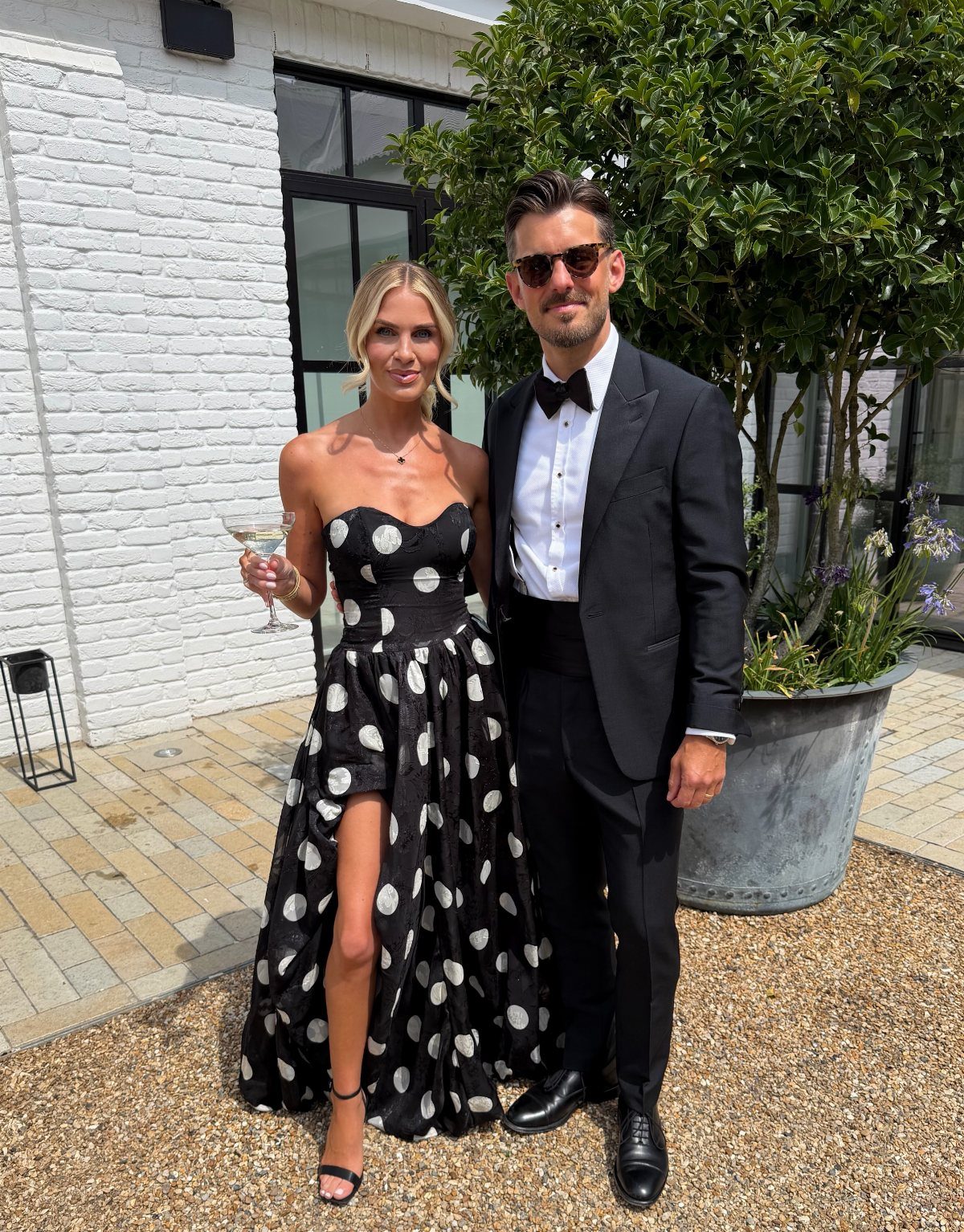 A woman wearing a black strapless polka dot dress standing next to a man in a tuxedo.