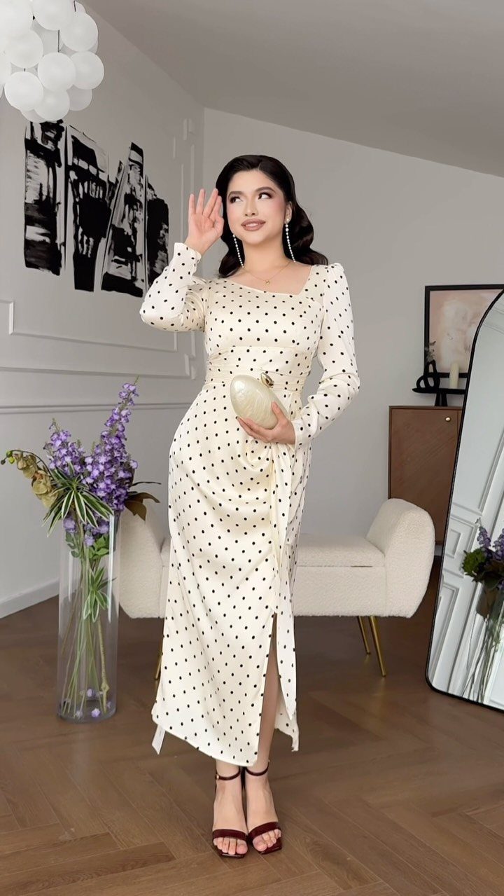 Woman in a cream polka dot midi dress posing in a modern living room.
