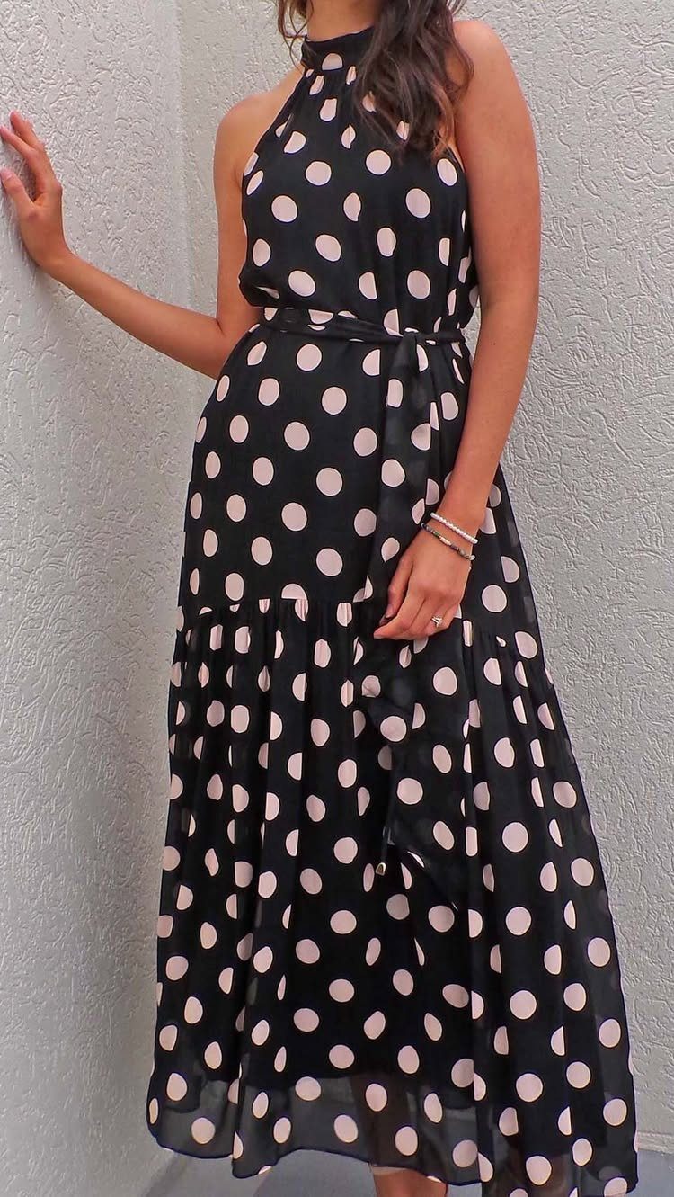 Woman wearing a black and white polka dot halter maxi dress with a ruffle hem.