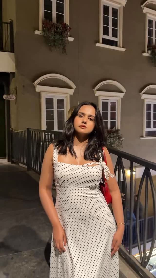 A woman wearing a white polka dot dress posing on a walkway at night.