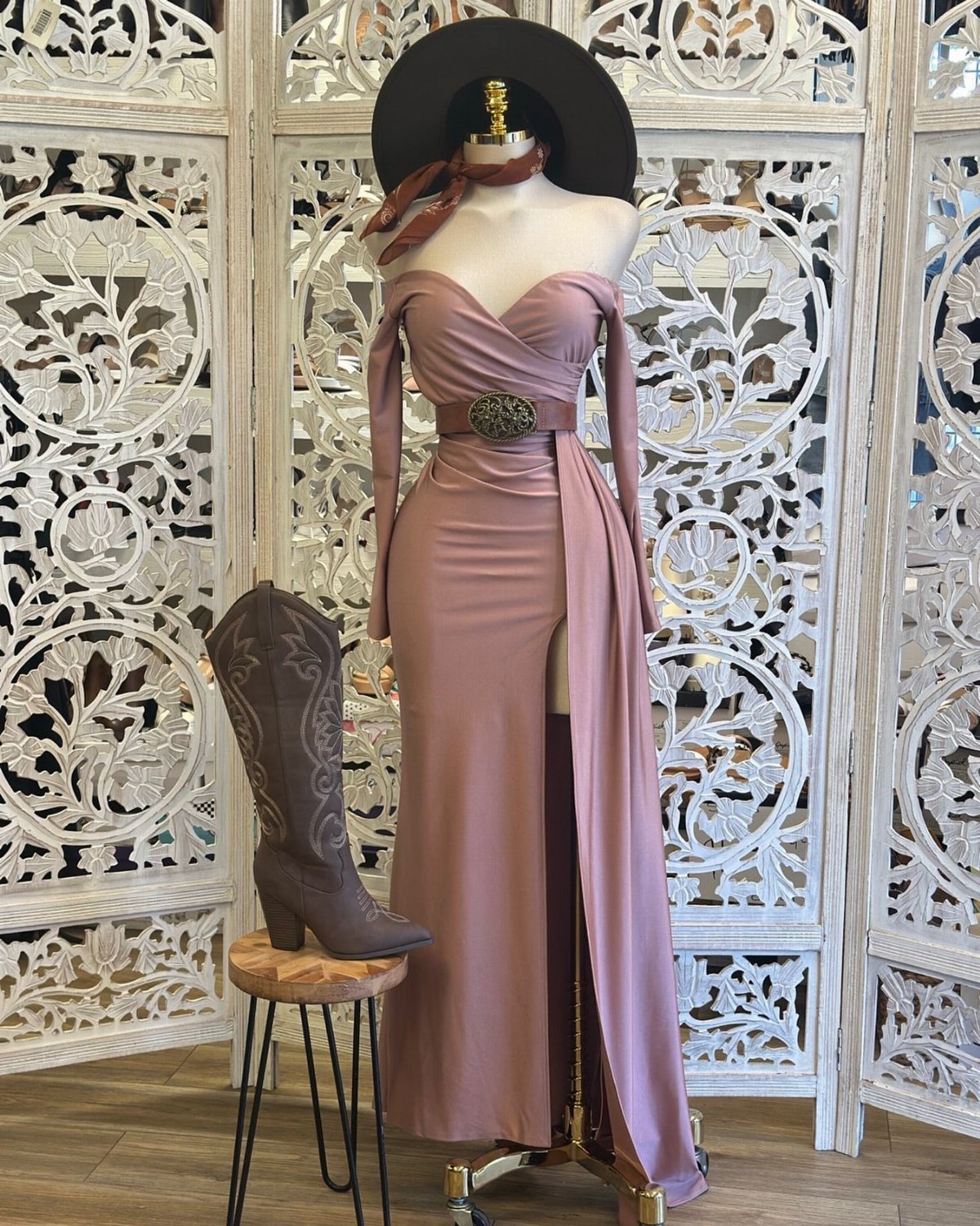 A mauve off-the-shoulder maxi dress on a mannequin with a brown leather belt and cowboy boot.