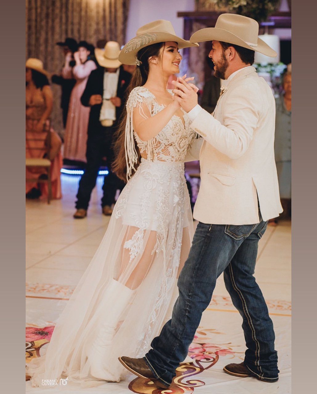 A bride in a lace wedding dress and a groom in cowboy hats dancing together.
