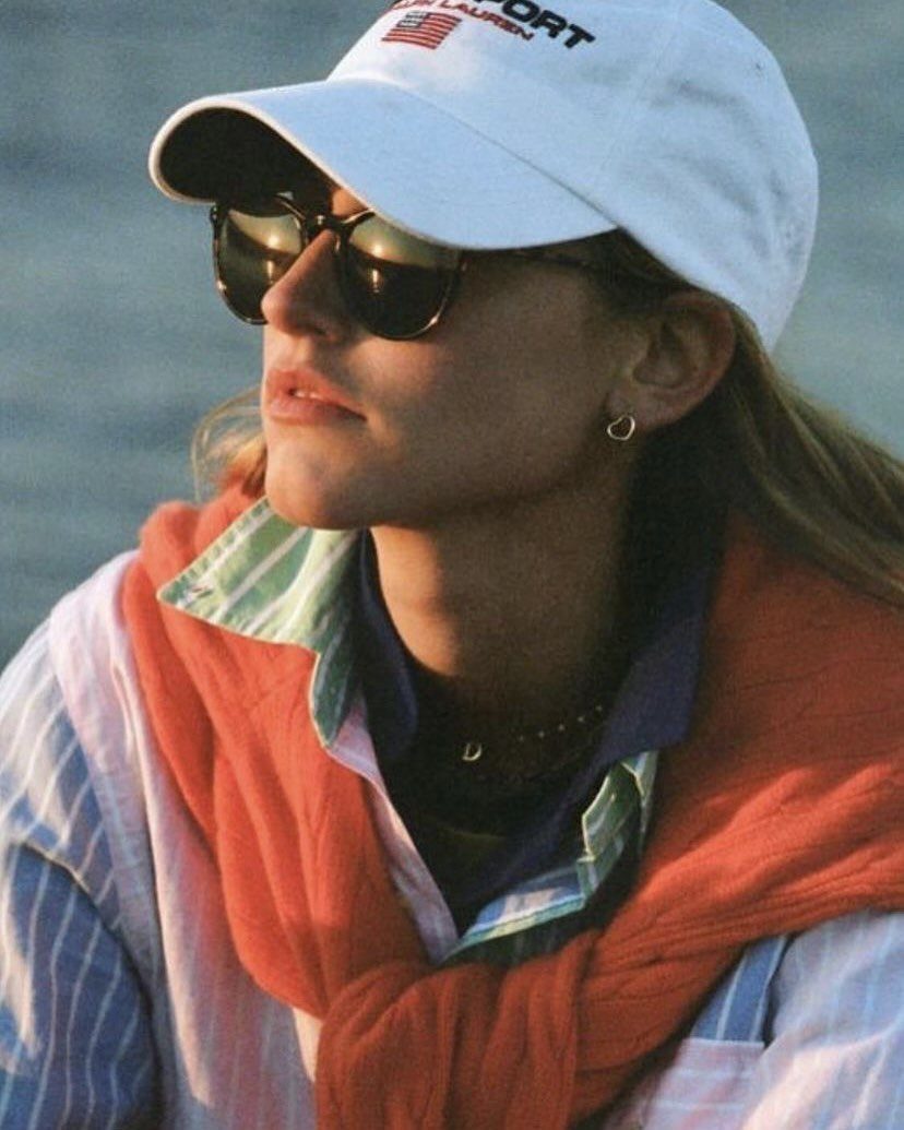 Woman in a white cap and sunglasses with a red sweater draped over her shoulders.