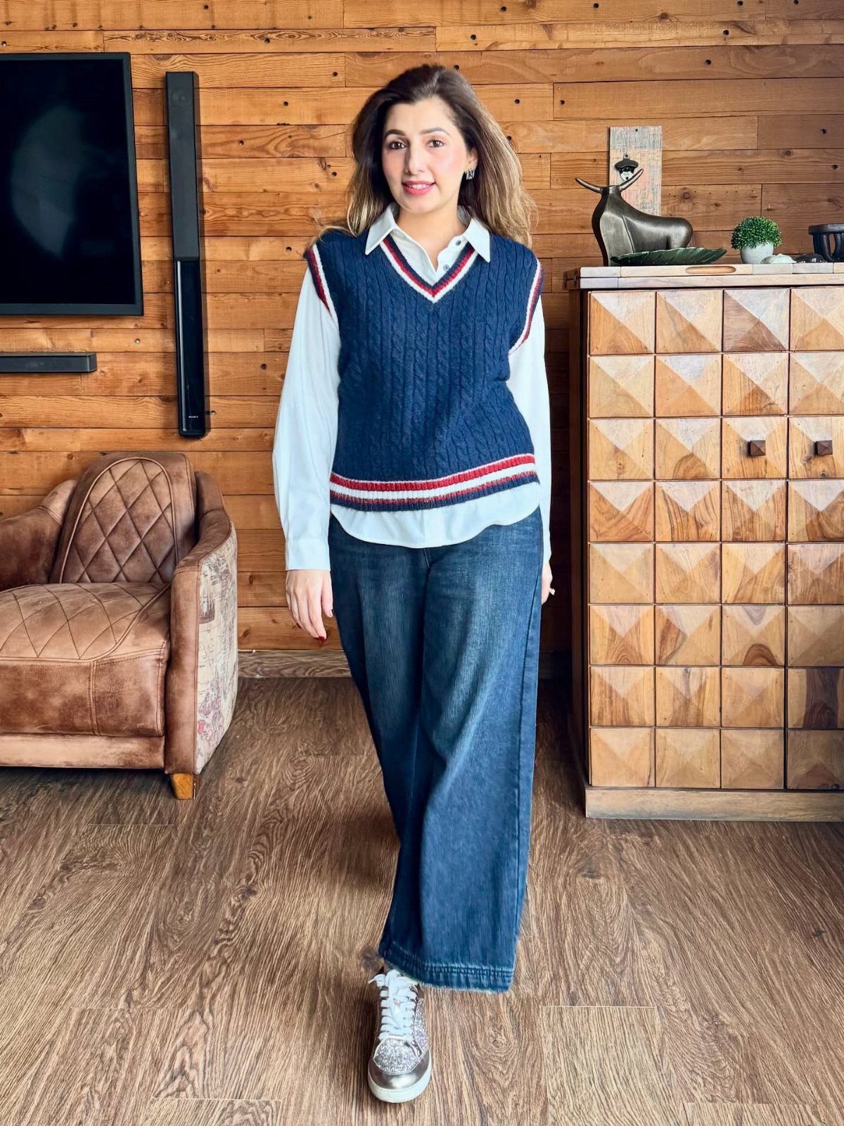 Woman wearing a blue sweater vest over a white shirt and wide-leg denim jeans.