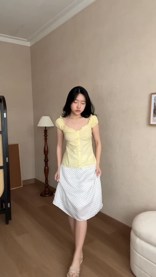 A woman wearing a yellow ruffled top and a white polka dot A-line skirt.