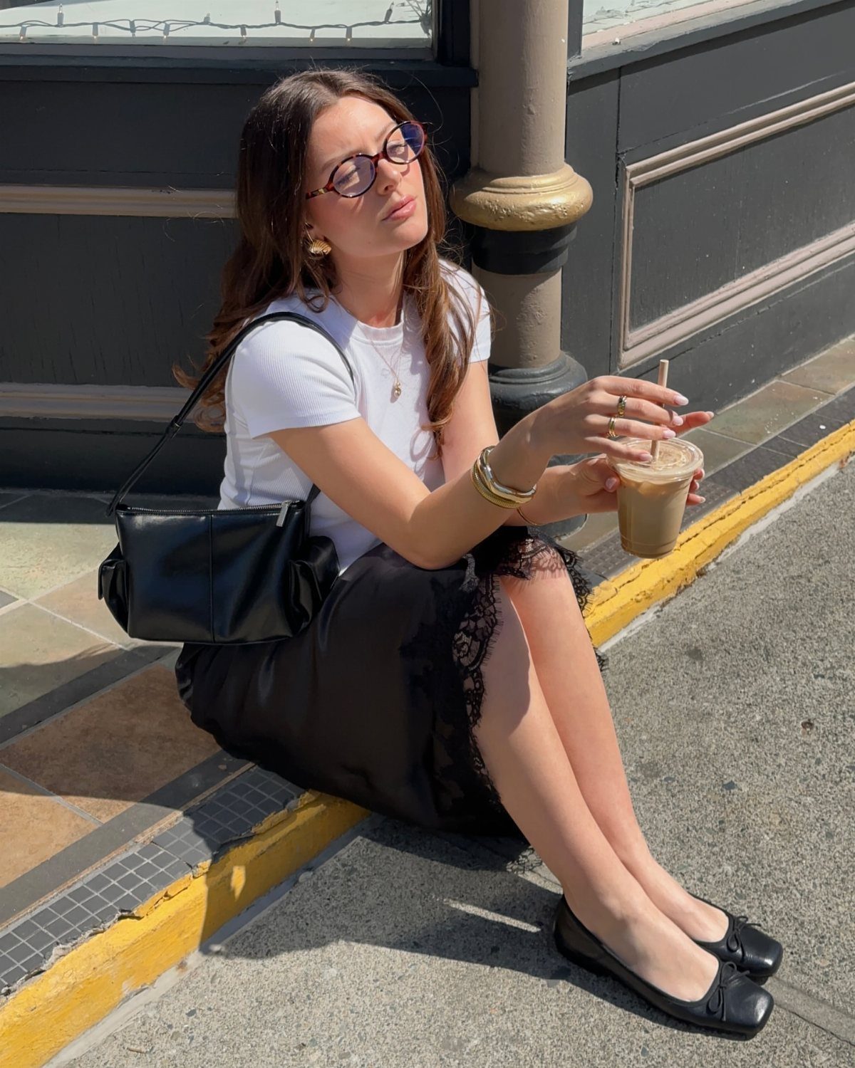 Woman sitting on a curb wearing a white t-shirt and a black lace midi skirt.