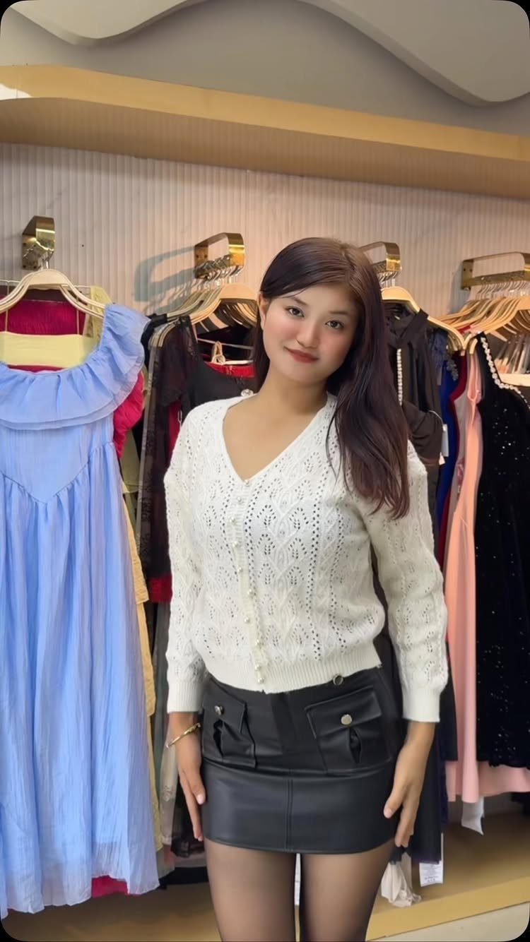 A woman wearing a white lace cardigan and black leather mini skirt in a clothing store.
