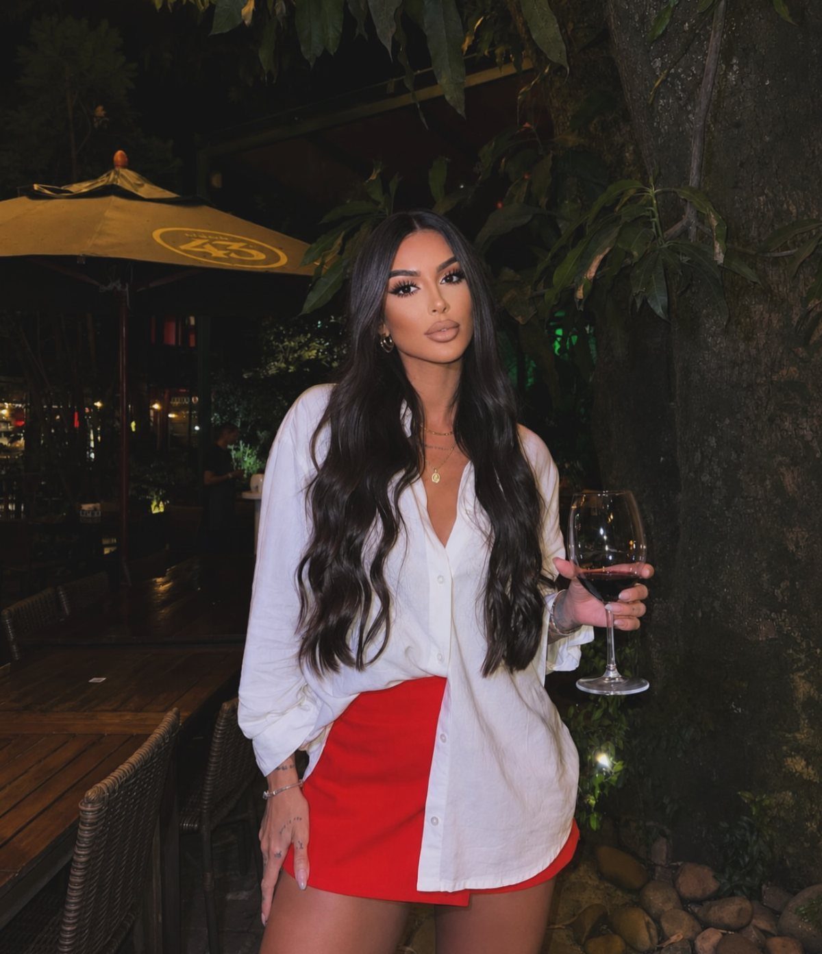 Woman in a white shirt and red mini skirt holding a glass of red wine.