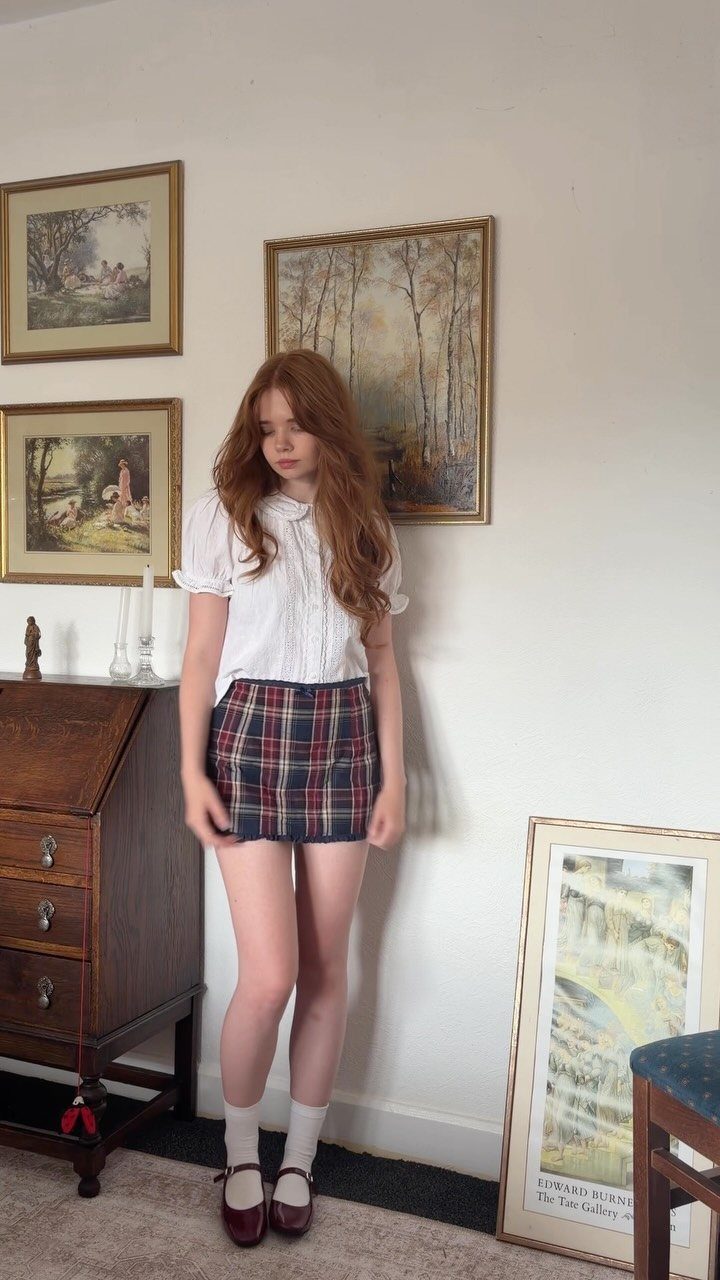 Red-haired woman wearing a white blouse and plaid mini skirt with white socks.