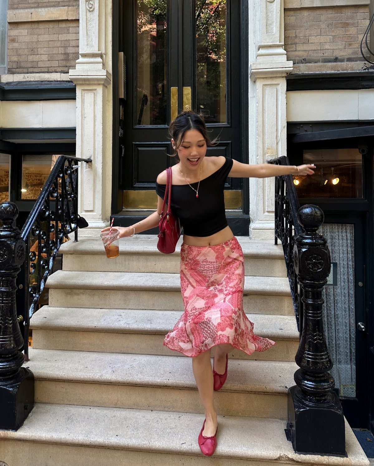 A woman in a black top and pink patterned midi skirt walking down outdoor stairs.