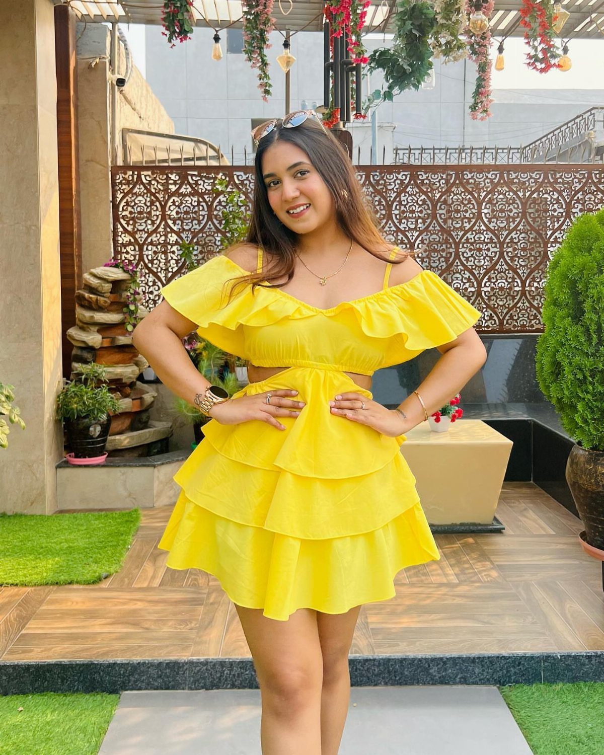A woman in a bright yellow ruffled mini dress posing on a patio.