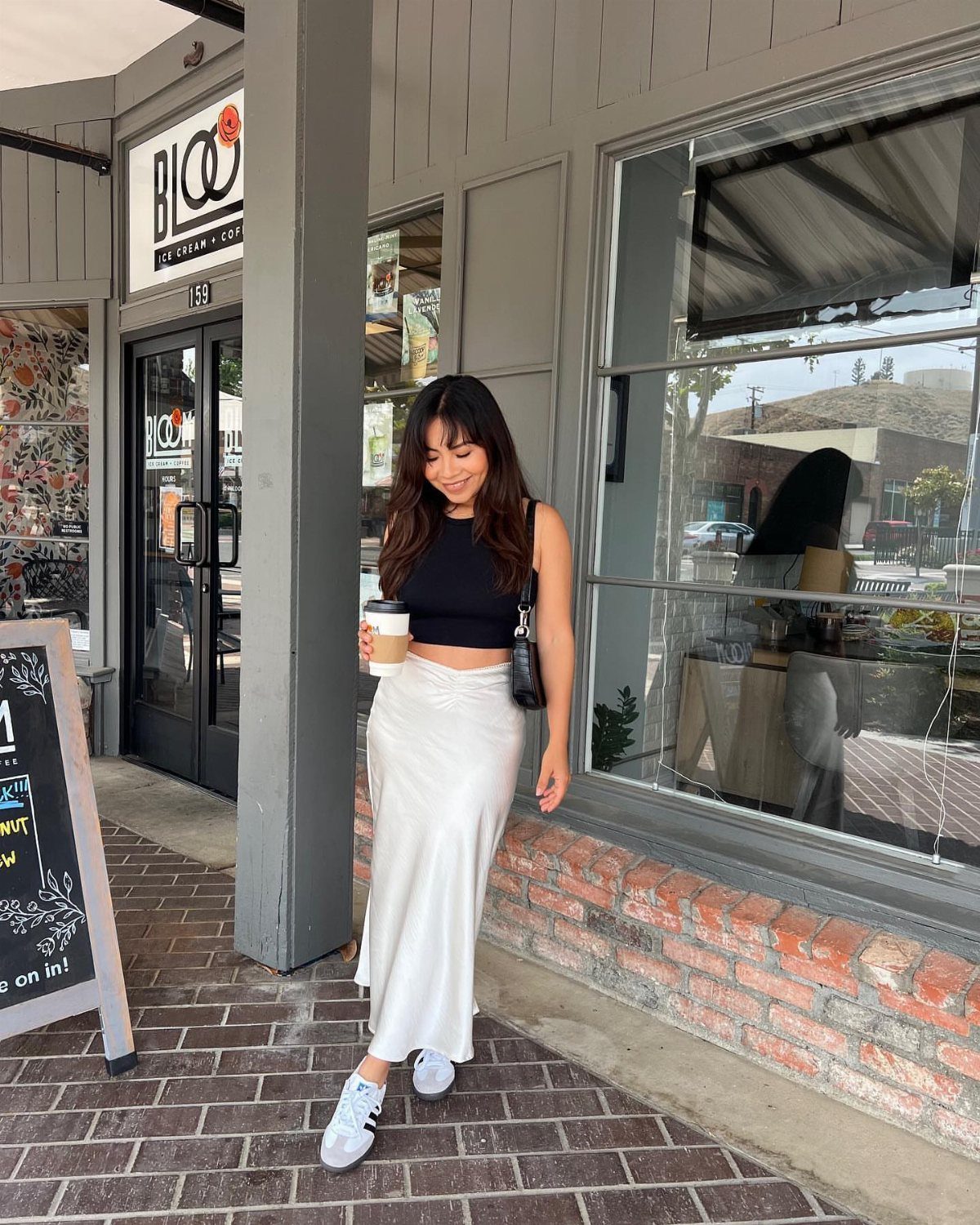 A woman wearing a white midi skirt and black crop top walking on a brick sidewalk.