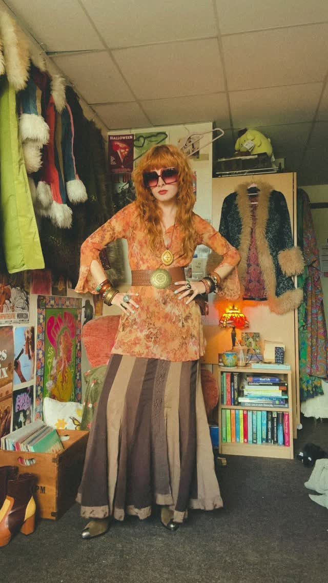 A person wearing a 70s boho chic outfit with an orange tunic and striped maxi skirt.
