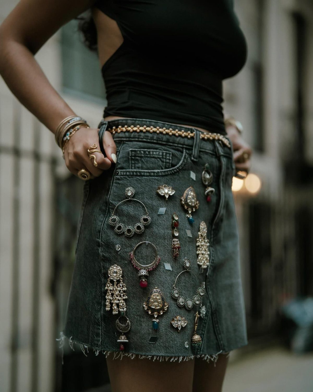Person wearing a black top and a denim skirt decorated with large ornate jewelry pieces.