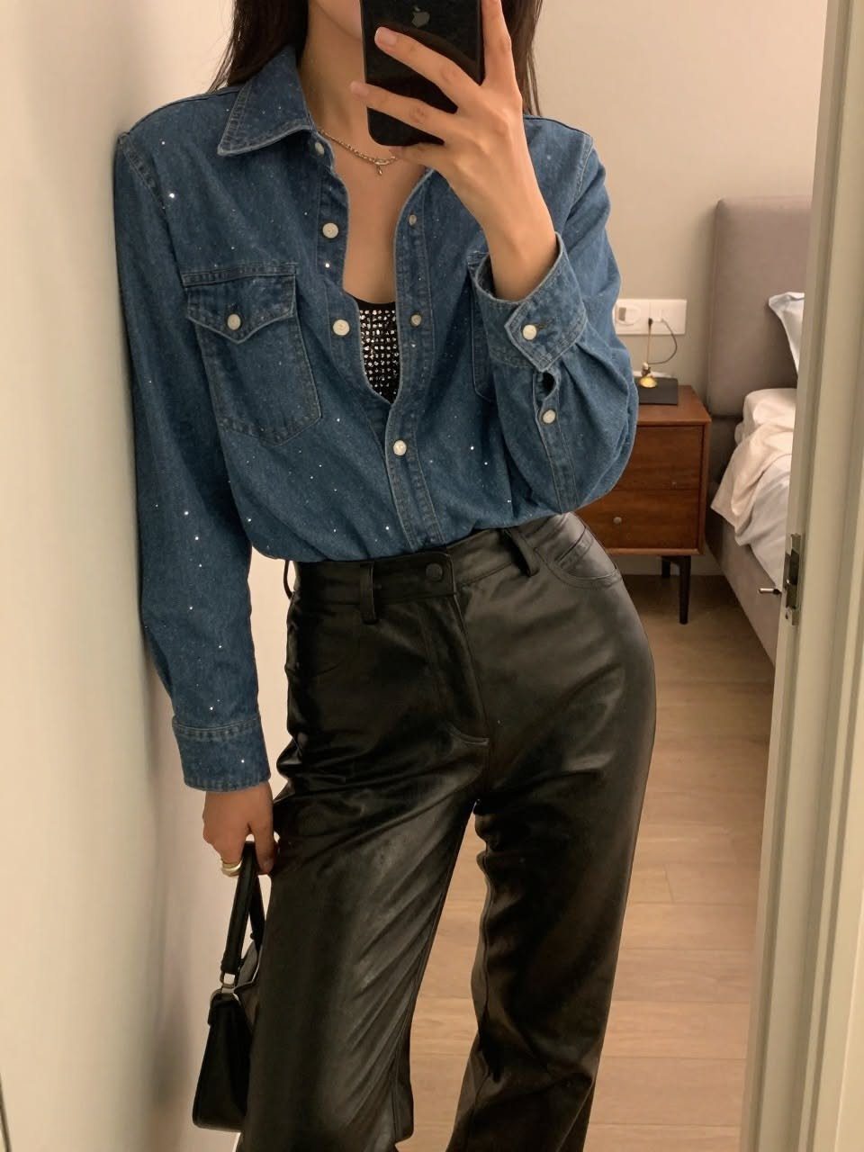 Person wearing a blue denim button-down shirt with rhinestone embellishments and black leather pants.