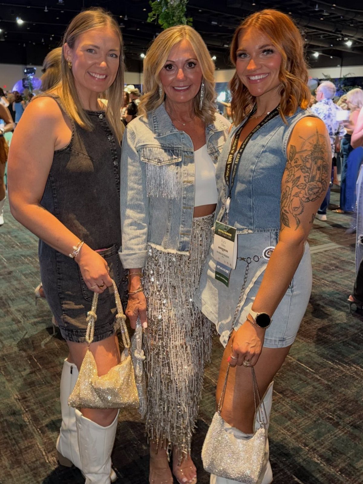 Three women posing together, one wearing a denim jacket and a long silver sequined skirt.